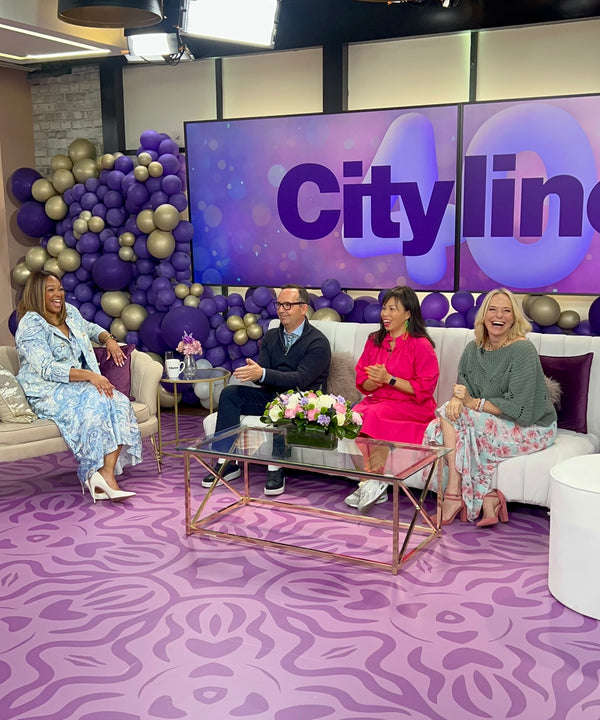 Image of Cityline studio decorated in iconic Cityline purple, with gold and purple balloons and a big purple carpet, host Tracy is sitting on a chair across from experts Frank Ferragine, Pay Chen and Julia Grieve who are seated on a big white couch